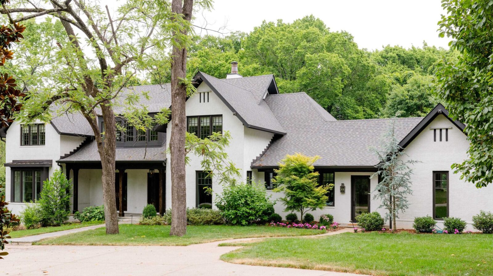 White cottage-style home with steep gables and black windows among mature trees