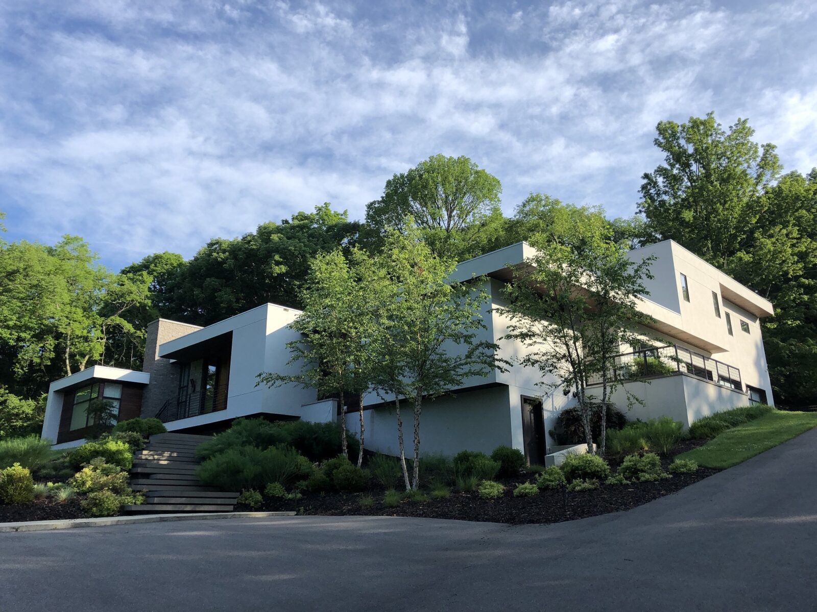 Modern white home with a cantilevered upper floor set into a wooded hillside